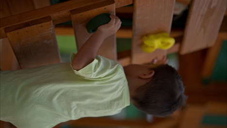 Vertikale-Zeitlupe-Eines-Jungen-Lateinamerikanischen-Jungen,-Der-Auf-Einem-Holzspielplatz-Klettert-Und-Sich-Voll-Auf-Die-Aufgabe-Konzentriert