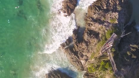 aerial top-down ascend view of waves crashing against rocks in byron bay, capturing the power and beauty of the ocean