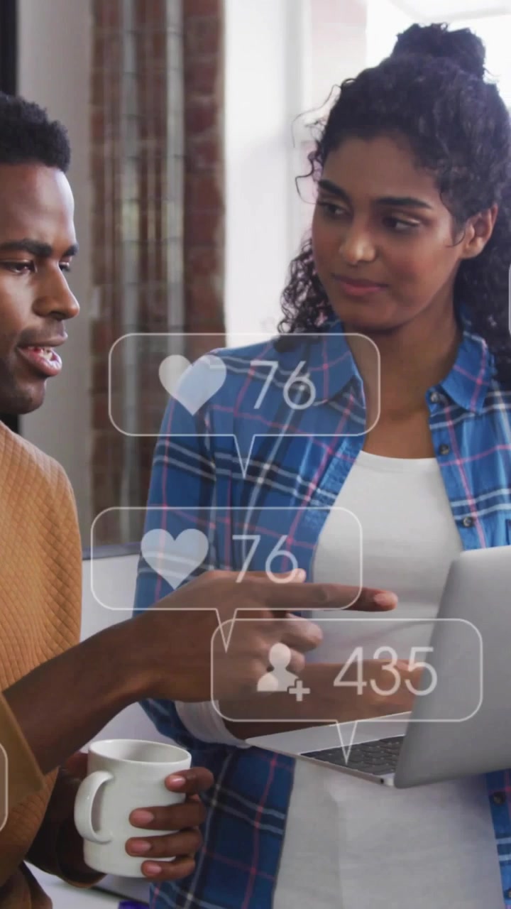 Vertical video: Woman tapping laptop, man with mug pointing, likes rising during marketing review