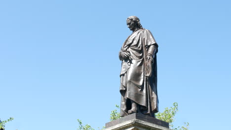 A-side-view-of-a-statue-of-the-mathematician,-physicist,-astronomer,-alchemist,-theologian,-and-author-Sir-Isaac-Newton-with-clear-blue-sky