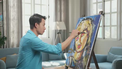 medium shot side view of an asian artist man holding paintbrush mixed colour and painting a girl's ear on the canvas