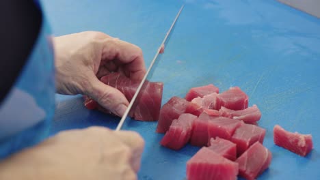 pescador que corta cubos de atún rojo para cocinar en superficie azul