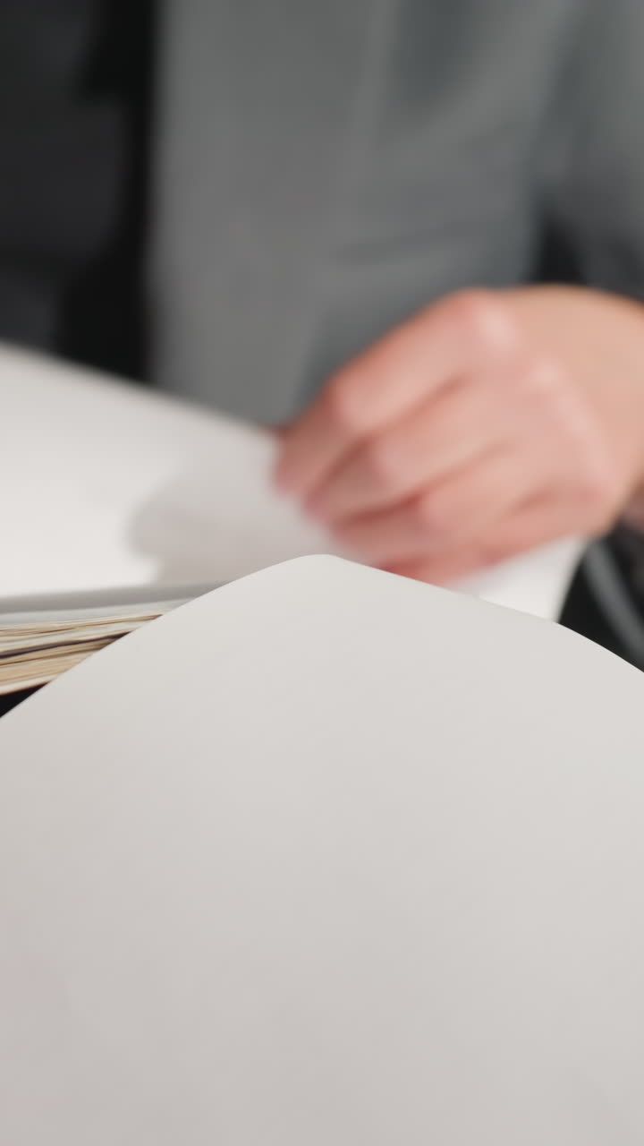 Businesswoman in gray suit reading document while sitting, pointing finger to page with thoughtful expression, possibly preparing for presentation or meeting, showing focus and concentration