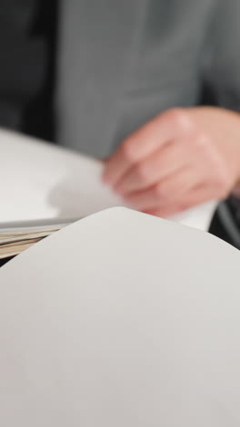 Businesswoman in gray suit reading document while sitting, pointing finger to page with thoughtful expression, possibly preparing for presentation or meeting, showing focus and concentration