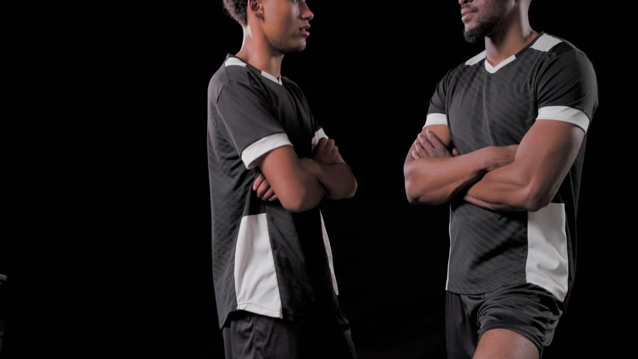 Afroamerikanska manliga lagkamrater sänker foten från fotbollen, korsar armarna och poserar i studio.