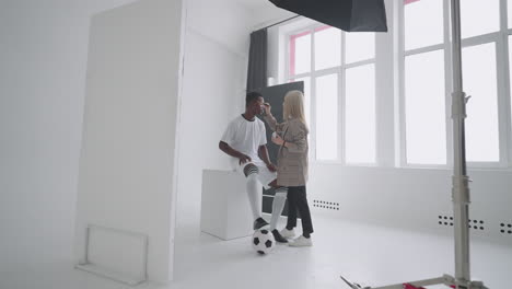 achter de schermen van een fotoshoot: een mooie zwarte model voetballer bereidt zich voor op een fotoshoot voor een tijdschrift een make-up artist corrigeert de huidskleur voor foto's in een sporttijdschrift
