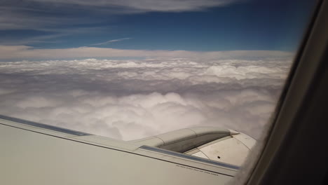 subjective view of a passenger in an airplane flying over a thick layer of white clouds under a blue sky