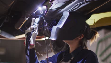 female mechanic wearing welding helmet welding under a car at a car service station