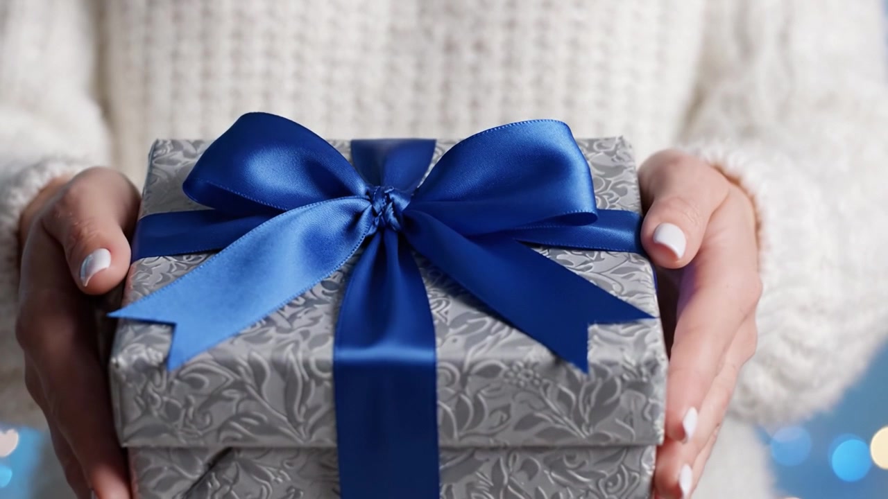 A beautifully wrapped gift box featuring an intricate design and a lovely blue ribbon, held with care by a person, embodying the spirit of giving and celebration.