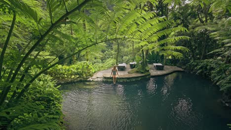 Mujer-Sentada-En-El-Borde-De-La-Piscina-Tropical-En-La-Selva-Creando-Ondas-En-La-Superficie-Del-Agua.