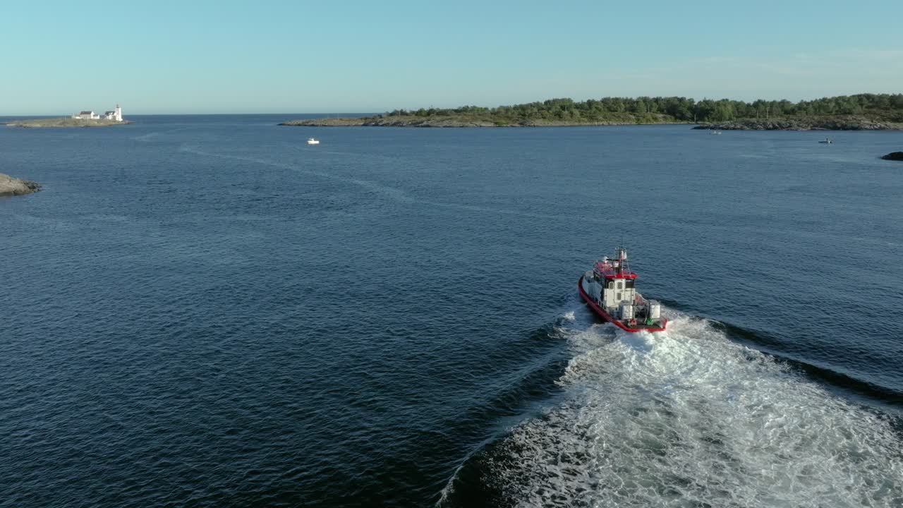 A tugboat speeds across smooth water, leaving a wake behind. Coastal islands are visible in the background, creating a serene maritime scene under clear skies