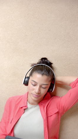 vertical video of biracial teenage girl on floor with headphones and phone, copy space, slow motion