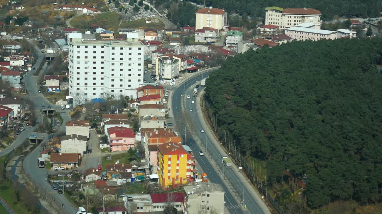 Aerial view of a city neighborhood with residential buildings and a road, surrounded by trees and forest.