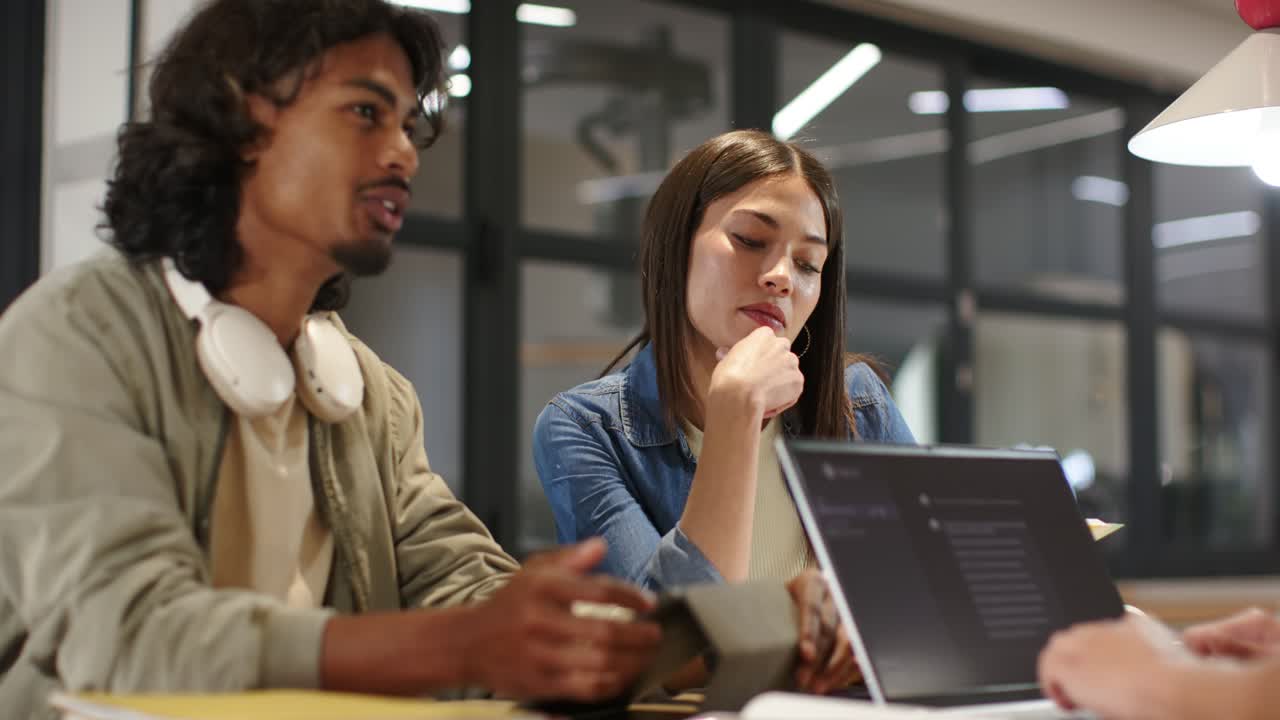 Diverse team man leading talk and gesturing woman listening seeking agreement with laptop at table