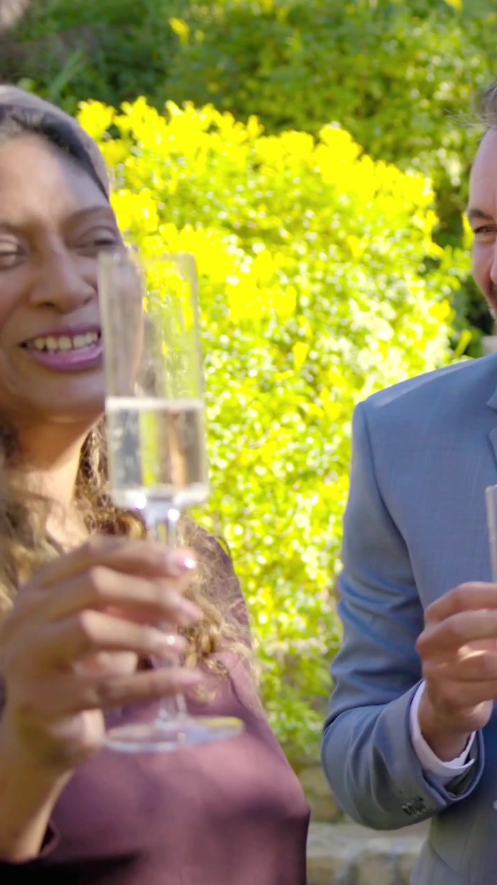 Vertical video: Man speaking raising flutes in garden, clinking, toasting with woman in purple top