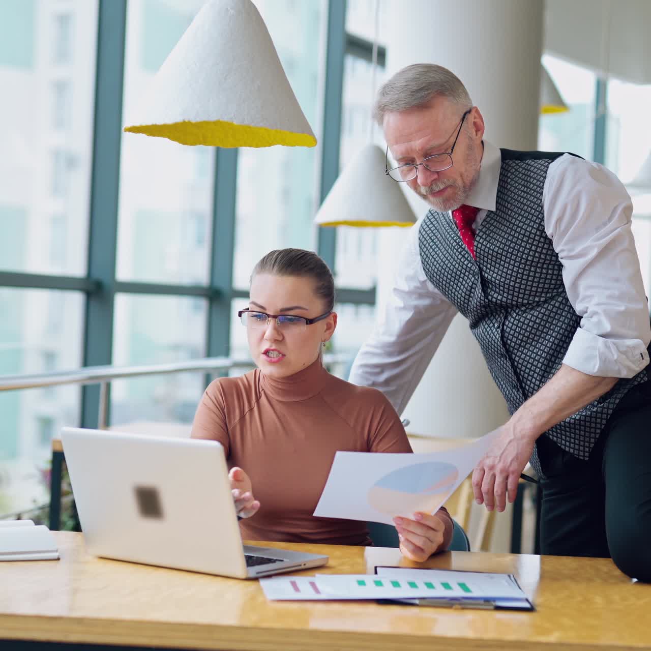 Mature entrepreneur and secretary in the modern company. Young woman in glasses talking with her chief and smiling.