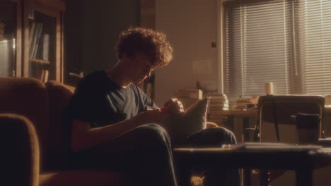 young depressed man sitting on sofa at home, looking at pill bottle