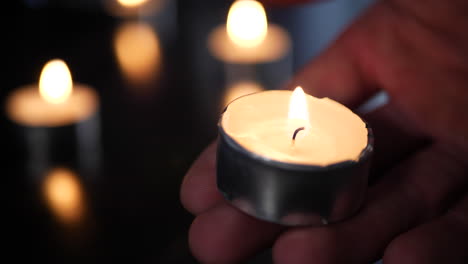 a hand holding a tealight candle on fire in a church temple with other candles burning and heavy background blur bokeh behind