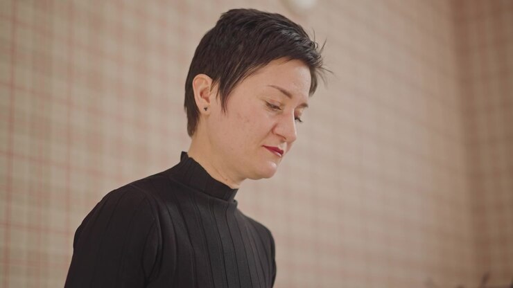 Insegnante di canto asiatica in un piccolo studio che ascolta attentamente la voce dello studente, valutando tono e postura alla tastiera, illuminazione calda e soffusa, atmosfera calma e concentrata, espressione ravvicinata che mostra concentrazione