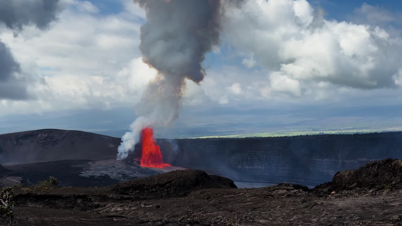 Lys rød lavafontæne bryder ud inde i Kilauea-krateret på Hawaii, med tyk røgsky, der stiger op over mørkt vulkansk landskab.