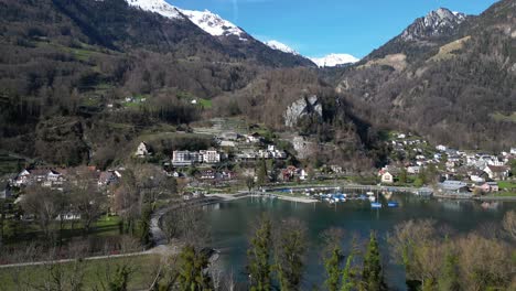 Drone-clip-of-traditional-Swiss-village-on-shore-of-Lake-Walensee,-surrounded-by-snowcapped-mountains