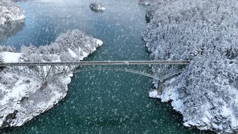 wide aerial view of deception pass bridge covered in snowfall with cars passing in-between islands