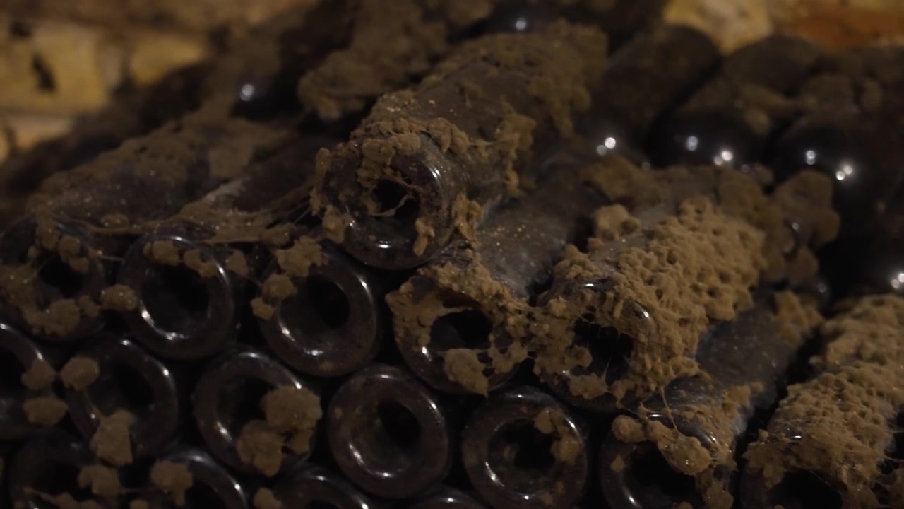 Very old, dusty, and moldy wine bottles stacked in a traditional dark underground wine cellar
