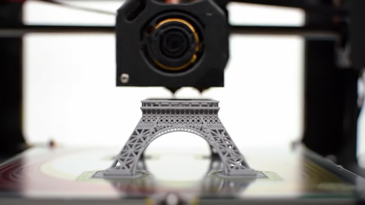 Watch as a small gray Eiffel Tower model is being printed using a 3D printer. The workshop showcases the technology involved in producing detailed miniatures in real-time.