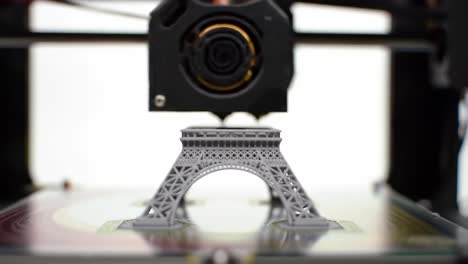 watch as a small gray eiffel tower model is being printed using a 3d printer. the workshop showcases the technology involved in producing detailed miniatures in real-time.