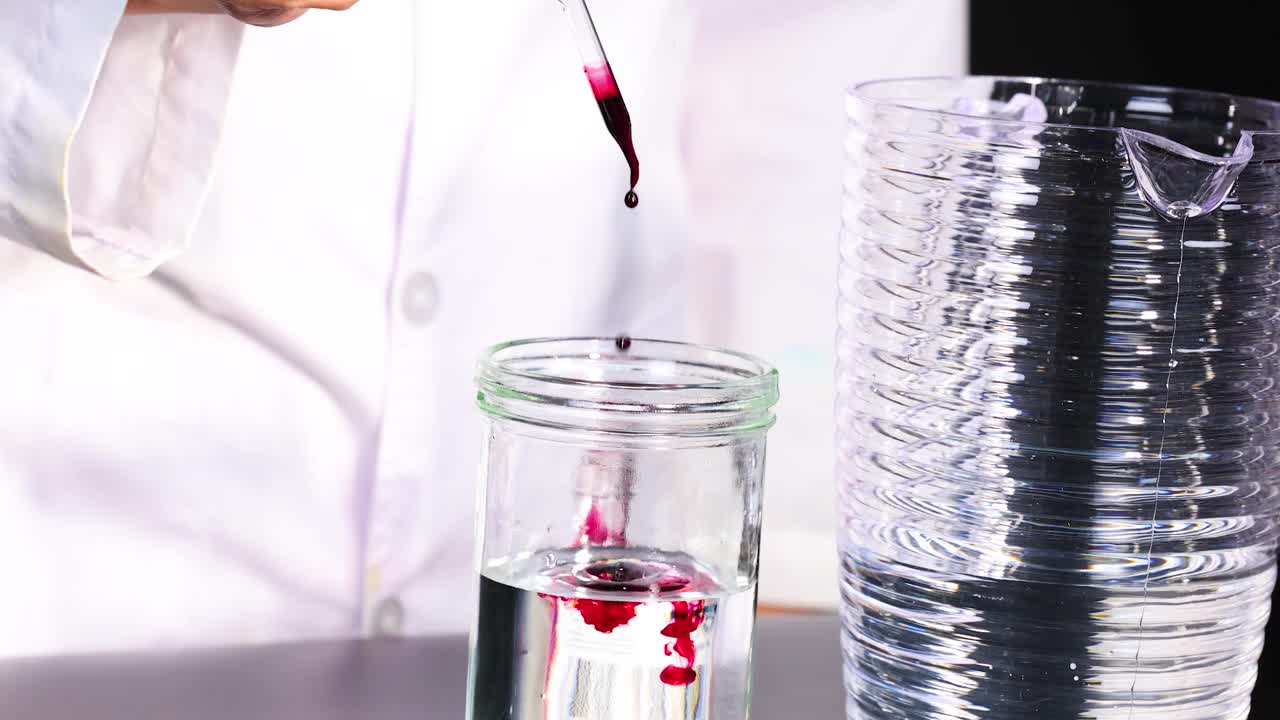 un científico agrega colorante alimentario rojo al agua, observando patrones de difusión en un entorno de laboratorio claro