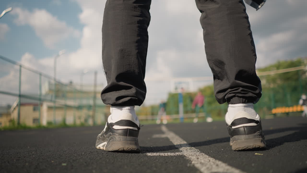 vista trasera de un atleta con zapatillas negras rebotando la pelota de voleibol en la cancha con figuras borrosas de tres personas en el fondo, rodeadas de vegetación