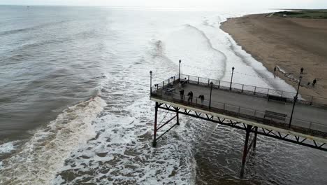 Typischer-Englischer-Badeort,-Aufgenommen-Mit-Einer-Drohne,-Die-Einen-Hohen-Luftbildpunkt-Bietet,-Der-Einen-Weiten-Sandstrand-Mit-Einem-Pier-Und-Tosenden-Wellen-Zeigt-1