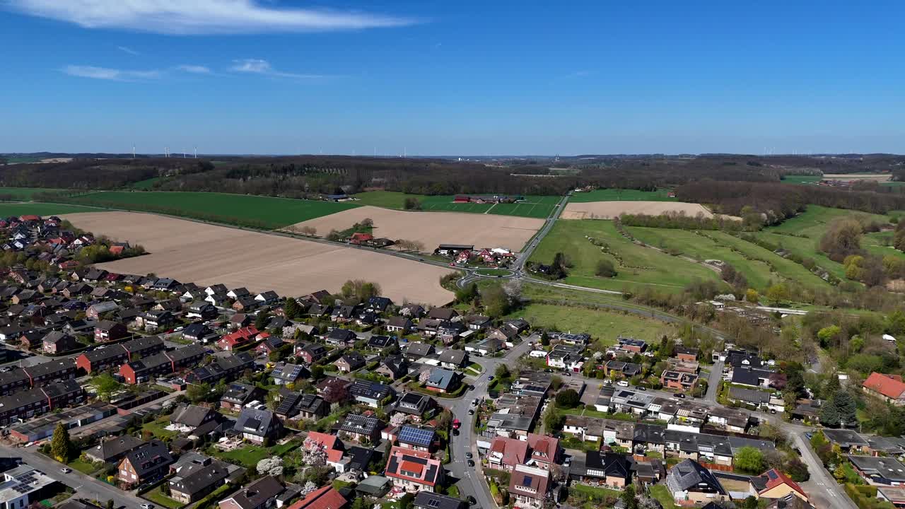 Hilly farm fields in small American town during sunlight in spring. Aerial lateral wide shot. American countryside district of town. Rooftops of houses and homes.