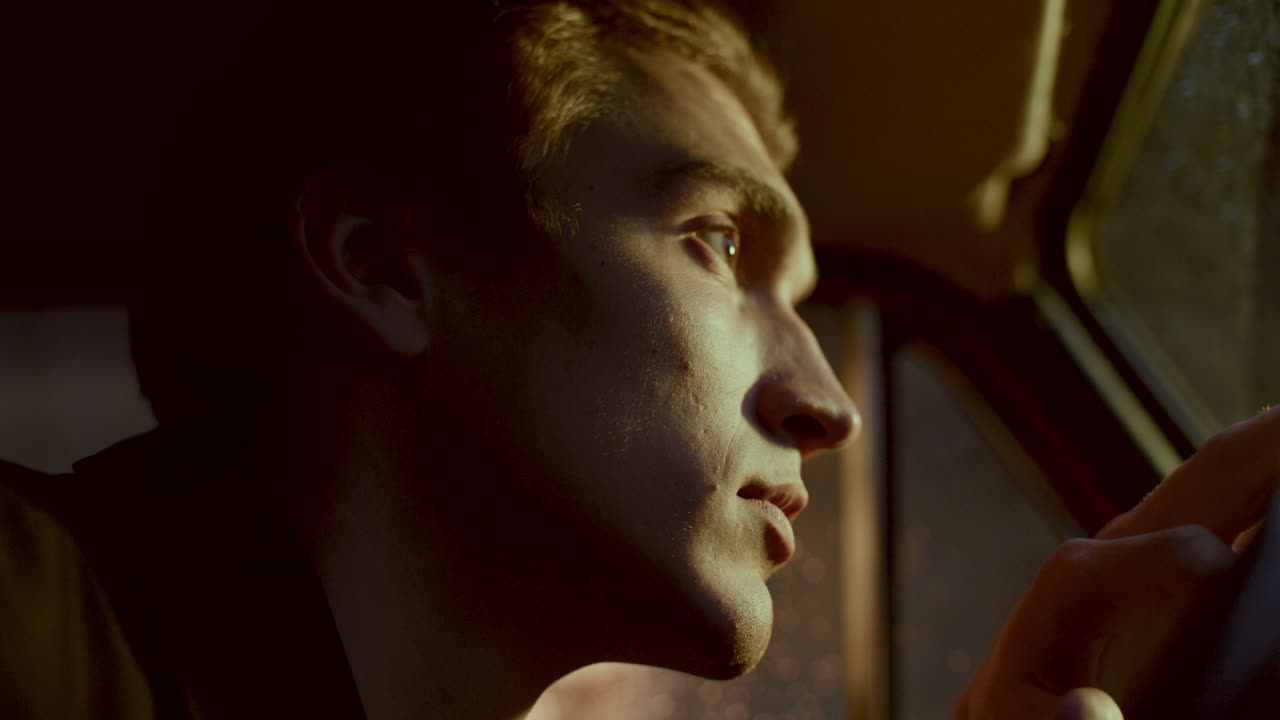 Man Resting Head on Steering Wheel, Reflecting Alone in Car at Night