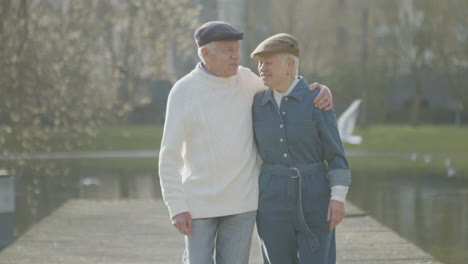 happy elderly couple walking along wooden pier in city park