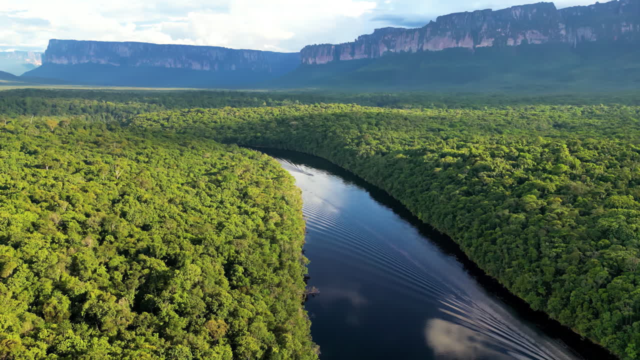 Aerial drone view of a boat moving along a dark rainforest river surrounded by dense tropical jungle in Venezuela