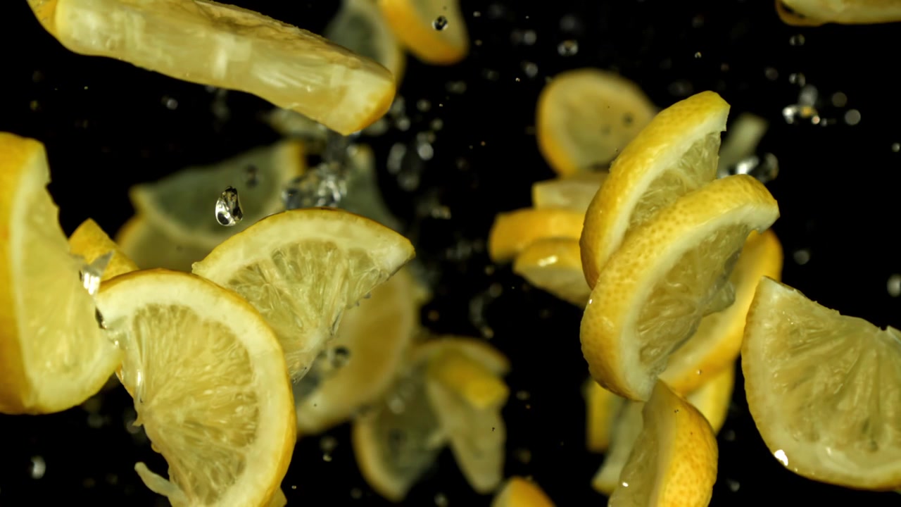 Fette di limone che cadono e schizzano con l'acqua su sfondo nero