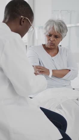 vertical video of diverse female doctor checking arm of senior female patient, slow motion