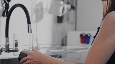 Housewife-hanging-cup-on-drying-rack-after-washing-in-kitchen-sink-at-home,-slow-motion