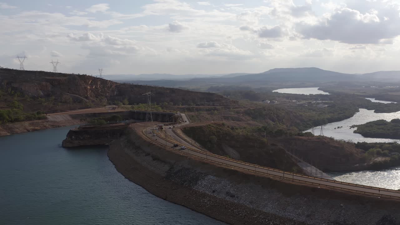 Orbiting left drone shot of cars passing by the Furnas Dam, a hydroelectric in Minas Gerais, Brazil, during a sunny day