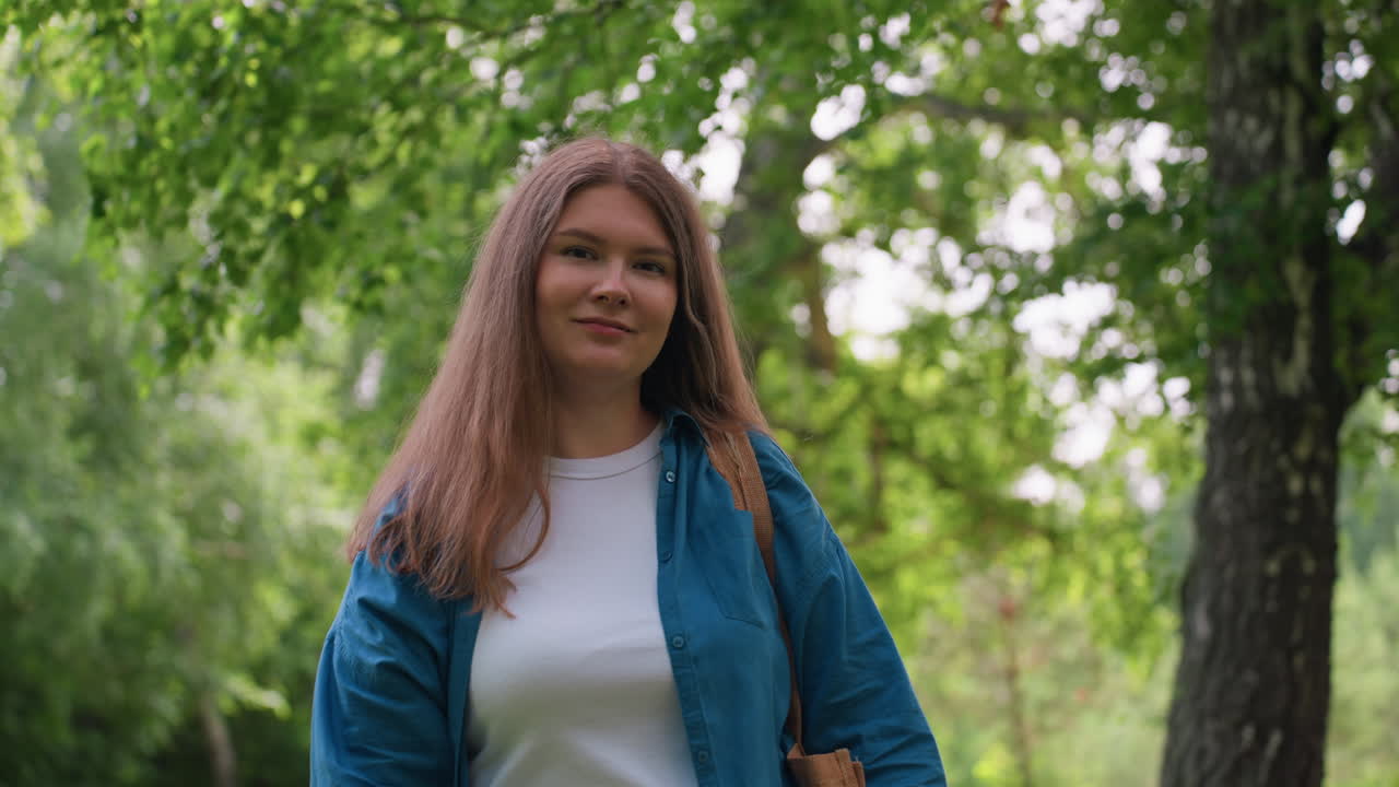 Tourist standing with warm smile in vibrant green park, wearing blue shirt and white top, surrounded by sunlight and trees, showing cheerful mood, peaceful energy, and relaxed confidence