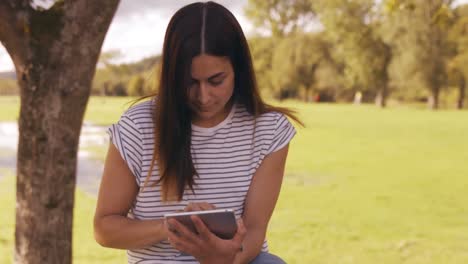 morena usando una tableta en un parque bonito