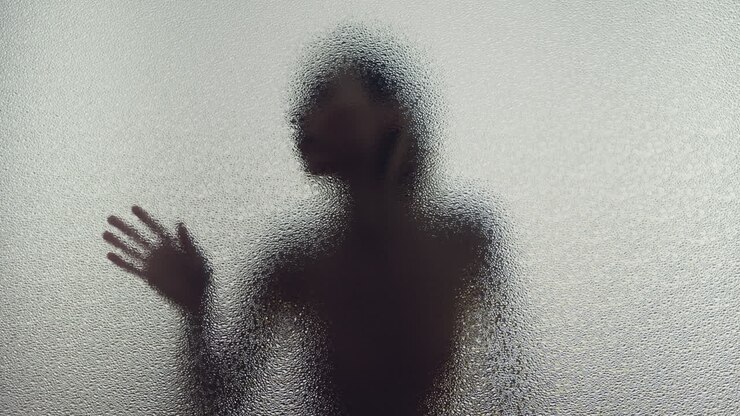 Una silhouette femminile dietro il vetro smerigliato si muove lentamente.