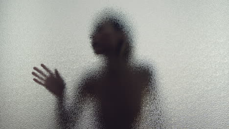 a female silhouette behind the frosted glass moves slowly