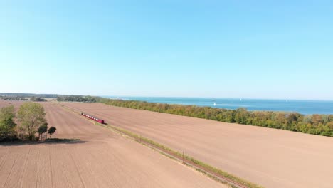 Aéreo:-Ferrocarril-De-Vía-Estrecha-A-Vapor-En-El-Campo-Pasando-Por-Campos-Sembrados-Y-El-Mar-Al-Fondo