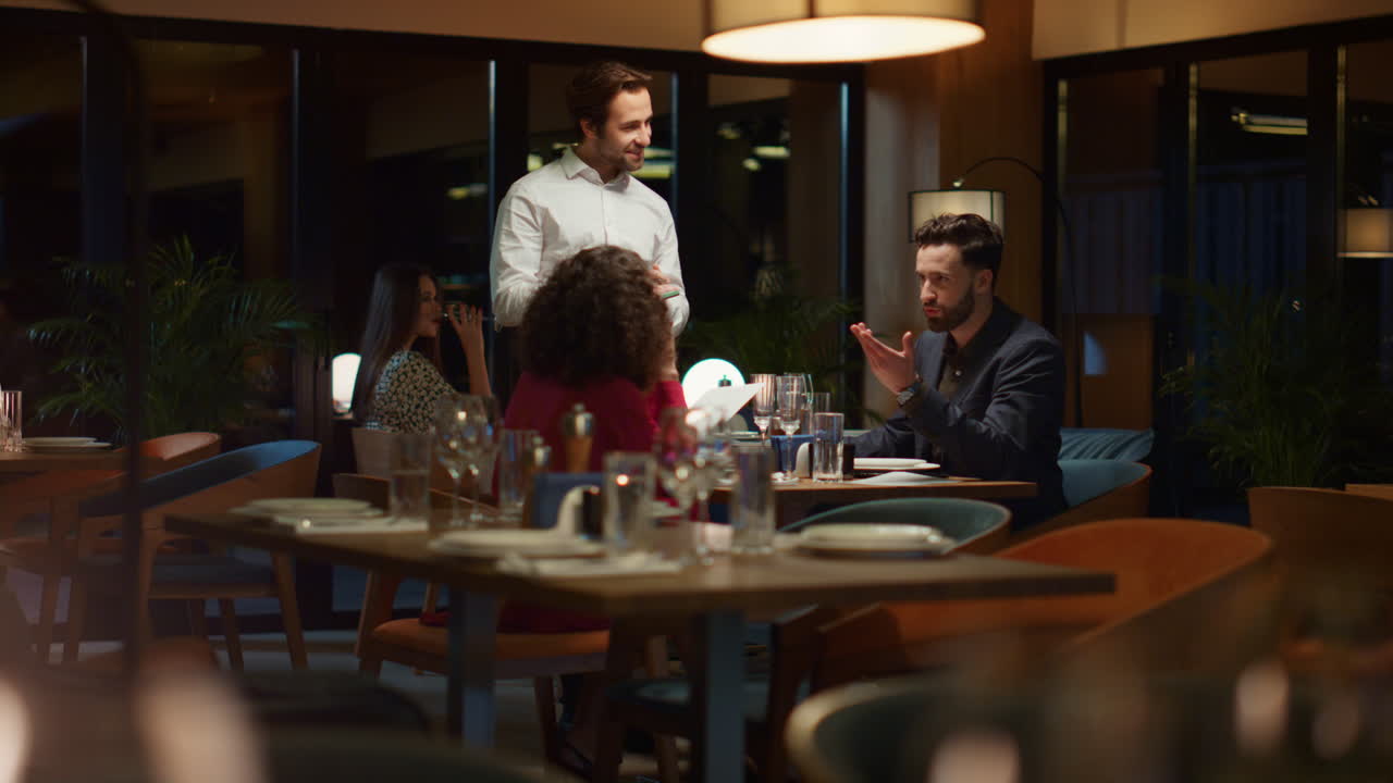 Waiter serving multiethnic couple on fancy restaurant dinner date at night.