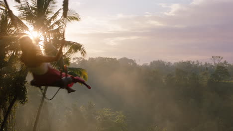 Mujer-Feliz-Balanceándose-Sobre-La-Jungla-Al-Amanecer-Viaje-Chica-Disfrutando-De-Vacaciones-Exóticas-En-Columpio-Con-El-Sol-Brillando-A-Través-De-Palmeras-En-La-Selva-Tropical-Libertad-De-Estilo-De-Vida-De-Vacaciones