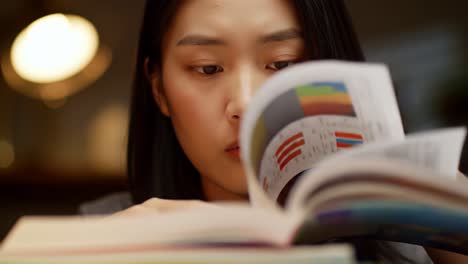 Young woman focuses intently on her studies, flipping through pages of textbooks and notes. Soft lighting creates a warm environment, perfect for late-night learning.