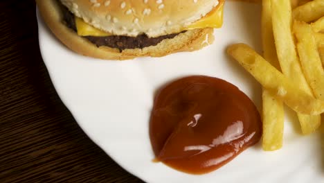 hand dipping fries in ketchup with a burger and fries