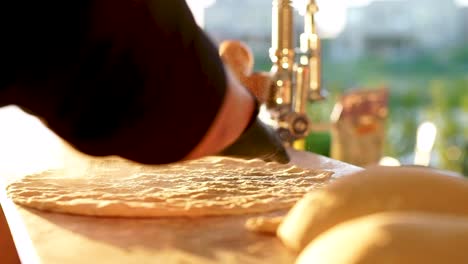 chef throwing flour on pizza dough, sunlit powder toss and spread with gloves, close up in slow motion